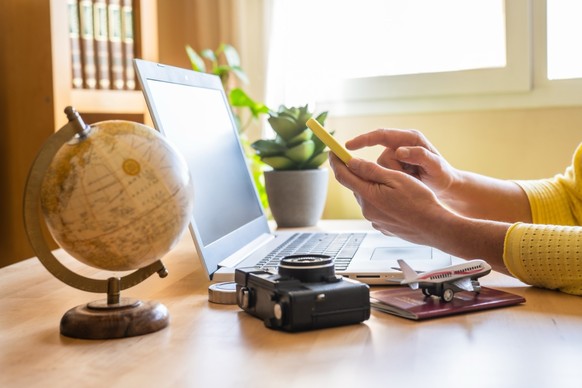 Frau mit Smartphone vor Laptop (Symbolbild, Reisen)