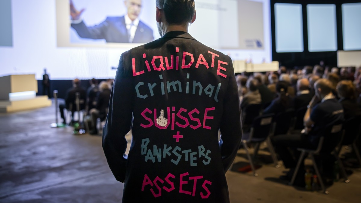 epaselect epa10558053 A man wears a suit with the writing "Liquidate Criminal Suisse + Banksters Assets" as Swiss bank Credit Suisse Chairman Axel P. Lehmann, back, speaks during the annual  ...