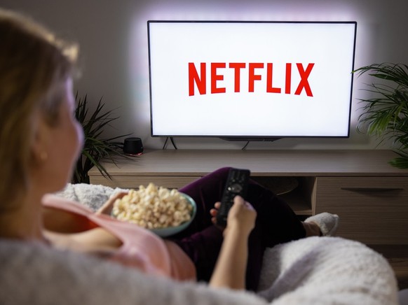 Woman holding popcorn and watching TV at home with Netflix logo on the screen.