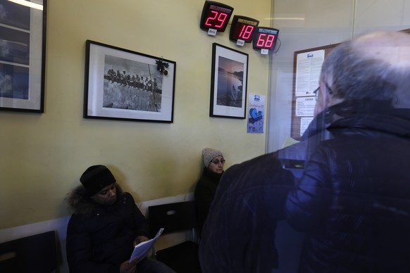 People are seen through a glass window as they wait inside a fiscal consultancy office to apply for the minimum income, in Rome, Wednesday, March 6, 2019. On Wednesday Italians are began queueing at p ...