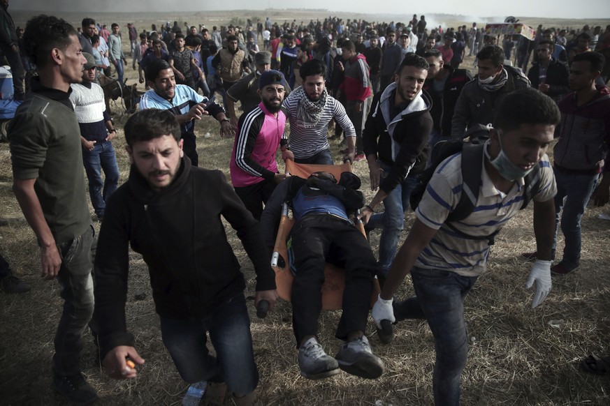 Palestinian protesters evacuate a wounded man during a protest at the Gaza Strip&#039;s border with Israel, Friday, April 13, 2018. (AP Photo/ Khalil Hamra)