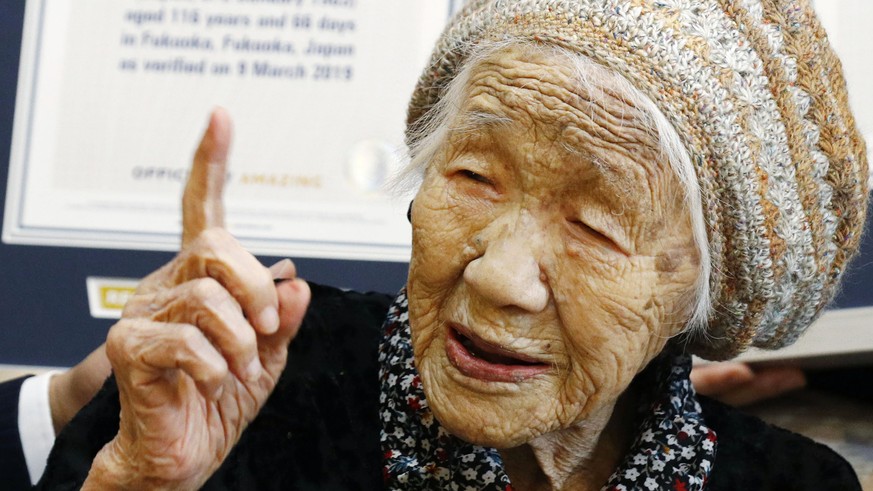 Kane Tanaka, a 116-year-old Japanese woman, gestures after receiving a Guinness World Records certificate, back, at a nursing home where she lives in Fukuoka, southwestern Japan, Saturday, March 9, 20 ...