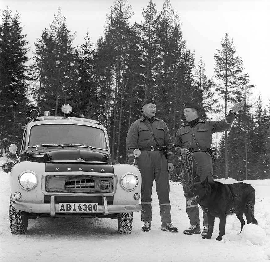 Polizisten mit Suchhund 1969. Zwei Polizisten mit einem Hund suchen und finden vermisste Personen in ihrem Polizeiauto, einem Volvo Duett. Das Modell wurde zwischen 1953 1969 hergestellt. Svahn Police ...
