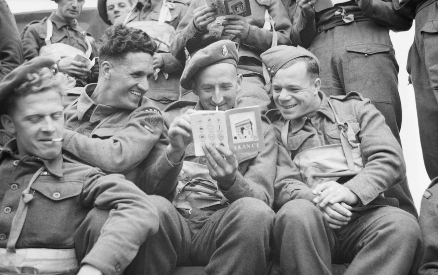 Operation Overlord the Normandy Landings- D-day 6 June 1944 The Final Embarkation: Three British soldiers of 51st Highland Division, aboard a landing craft, pass the time by reading the booklet on Fra ...