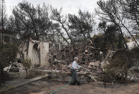 A woman sprays water outside her house that was damaged in the wildfires near the village of Neos Voutzas near Athens, Tuesday, July 24, 2018. Greece sought international help through the European Uni ...