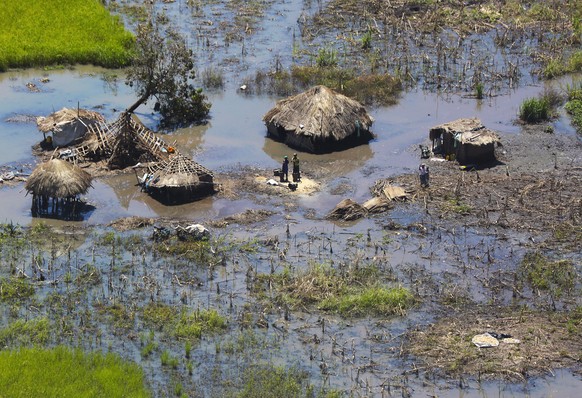 FILE - In this Tuesday March 26, 2019 file photo, a family stand outside their submerged huts near Beira, Mozambique. Beira&#039;s mayor Davis Simango dreamed about protecting his people from climate  ...