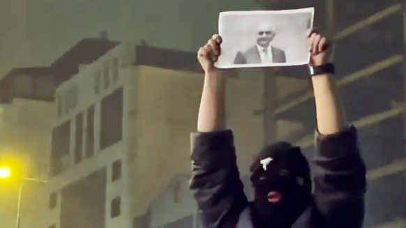 In this frame grab from video obtained by the AP outside Iran, a masked demonstrator holds a picture of Iran's Crown Prince Reza Pahlavi during a protest in Tehran, Iran, Friday, January. 9, 2026 ...