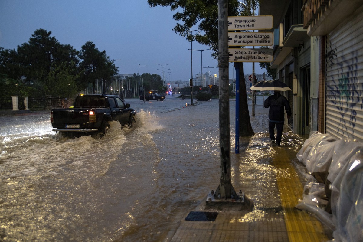 epa10886773 Vehicles and a resident cross a flooded street during a storm in Volos, central Greece, 27 September 2023. Residents of Volos in the Magnissia prefecture were ordered to stay indoors by po ...