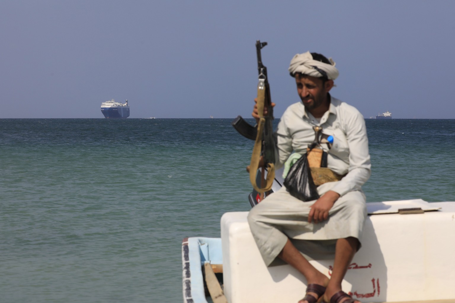 epa11012837 An armed Yemeni sits on a boat in front of the Galaxy Leader cargo ship, seized by the Houthis offshore of the Al-Salif port on the Red Sea in the province of Hodeidah, Yemen, 05 December  ...