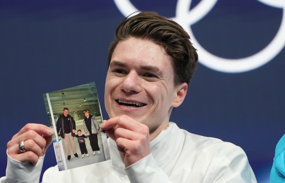 Maxim Naumov of the United States waits for his scores while holding a photo of his parents after competing during the men's figure skating short program at the 2026 Winter Olympics, in Milan, It ...