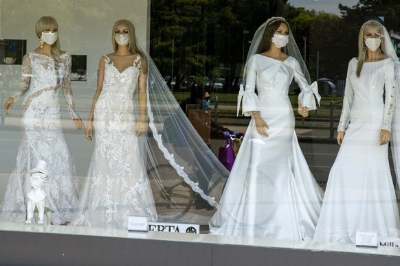 FILE - A masked cyclist is reflected in the window of a wedding dress store with mannequins wearing face masks, in Zagreb, Croatia on April 23, 2020. Now that weddings have slowly cranked up under a p ...