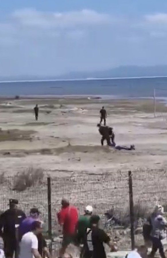 Sicherheitsleute zerren einen Demonstranten über den Strand. Demonstranten werden mit Sicherheitszäunen vom Meer abgehalten.