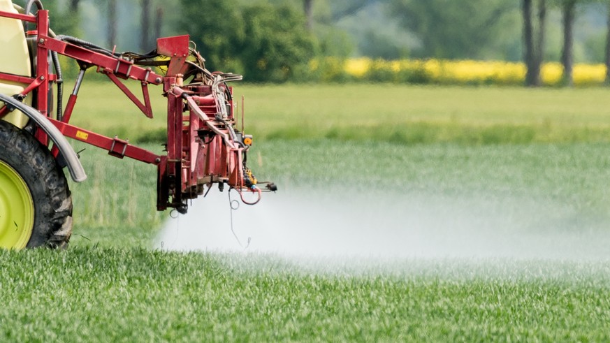 Ein Bauer fährt mit einer Dünger- und Pestizidspritze über ein Feld.