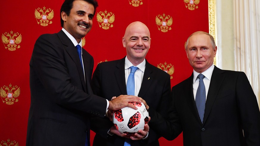 epa06889816 Emir of Qatar Sheikh Tamim bin Hamad Al Thani (L), Russian President Vladimir Putin (R) and FIFA President Gianni Infantino (C) pose with a ball during a symbolic ceremony of transferring  ...