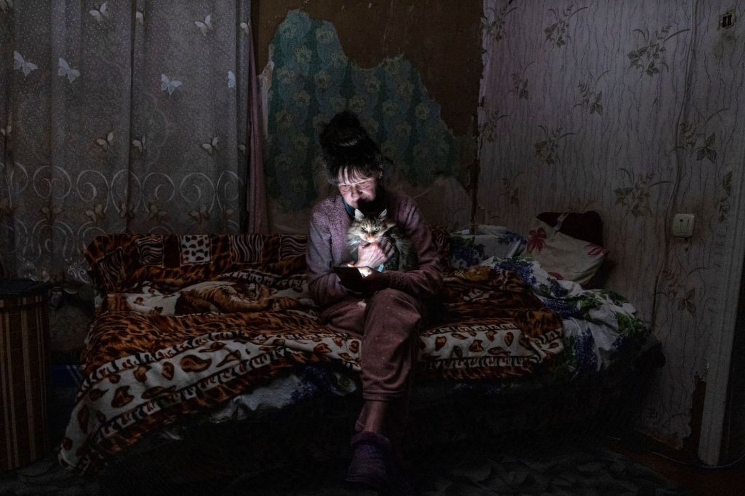 BORODYANKA, UKRAINE - OCTOBER 20: Tetyana Safonova, 61, sits with her cat Asya as she looks at her mobile phone during a power outage on October 20, 2022 in Borodyanka, Ukraine. Tetyana wasn't ab ...