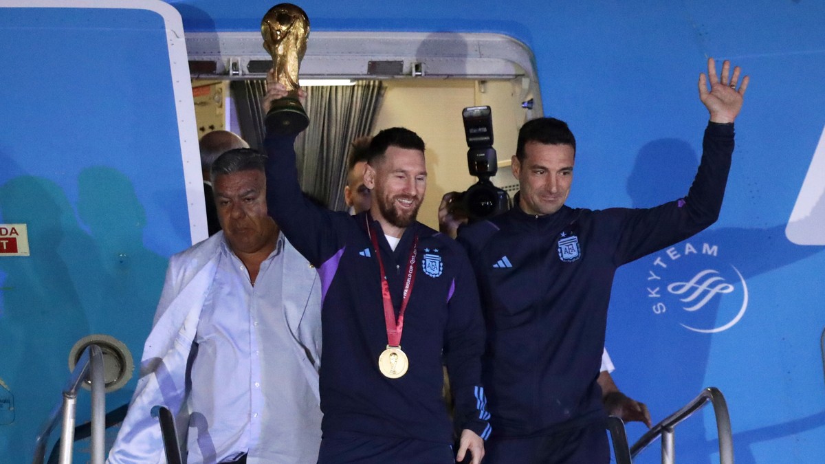 epa10374424 Lionel Messi (C) of the Argentina national soccer team descends a plane with the trophy of Qatar 2022 World Cup accompanied by head coach Lionel Scaloni (R), upon ther arrival to the Inter ...