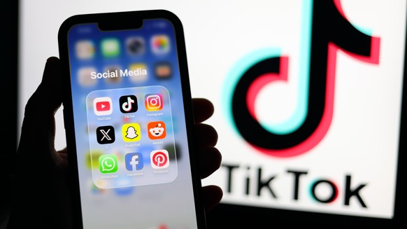 epa12674702 Social media applications displayed on a mobile phone alongside the TikTok logo displayed on a laptop screen in Liverpool, Britain, 23 January 2026. A proposal to ban under-16s from access ...