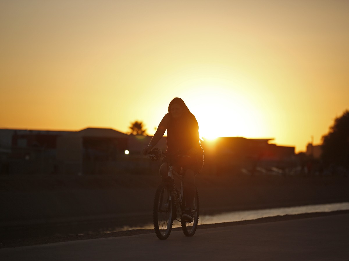 A woman rides her bicycle next to the Grand Canal as a very hot day ends in Phoenix, Thursday, July 6, 2023. The high temperature in Phoenix, Thursday hit a maximum of 115 degrees Fahrenheit (46.1 deg ...