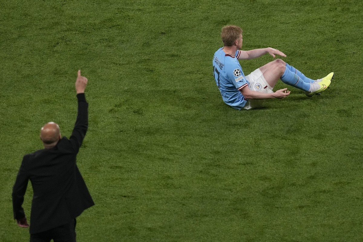 Manchester City's Kevin De Bruyne lies on the pitch following a challenge as Manchester City's head coach Pep Guardiola gestures during the Champions League final soccer match between Manche ...