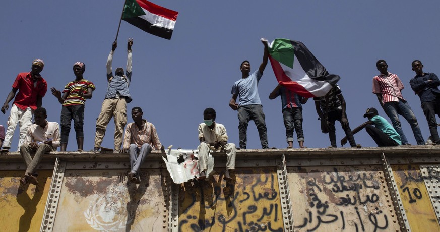 FILE - In this May 2, 2019, file photo, Sudanese protesters wave national flags at the sit-in outside the military headquarters, in Khartoum, Sudan. Explosions and machine gunfire were heard in Sudan& ...