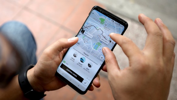 epa06631485 A man looks for an Uber car on his mobile phone in Hanoi, Vietnam, 27 March 2018. Uber has agreed to sell its Southeast Asian operations to Grab. Uber will get a 27.5 percent stake in Grab ...