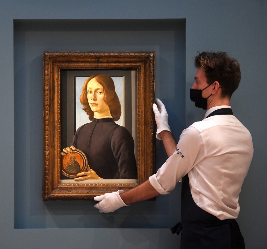 epa08856618 A Sotheby&#039;s staff adjusts the painting &#039;Young Man Holding a Roundel&#039; by Renaissance Italian artist Sandro Botticelli at a press preview at Sotheby&#039;s auction house in Lo ...