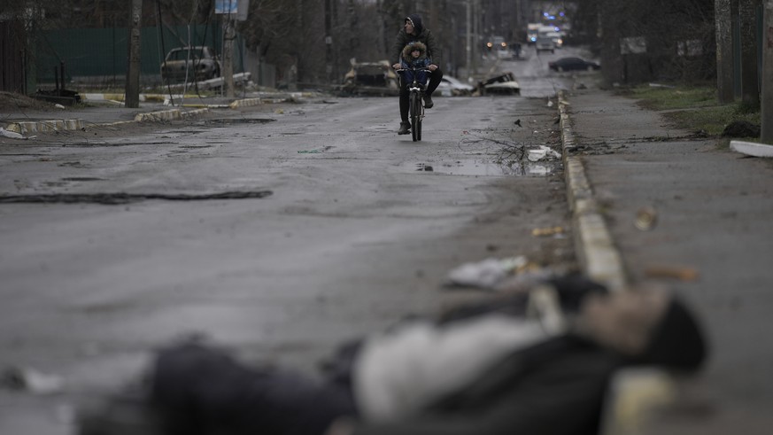 A man and child on a bicycle come across the body of a civilian lying on a street in the formerly Russian-occupied Kyiv suburb of Bucha, Ukraine, Saturday, April 2, 2022. (AP Photo/Vadim Ghirda)