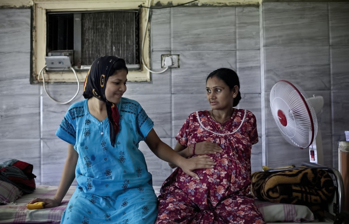 In this Nov. 2, 2015 photo, 30-year-old Bhagwati Chauhan, who gave birth to a Canadian couple's child on Oct. 27, touches the 9-month pregnant belly of 35-year-old Chandrika Makwana, who is carry ...