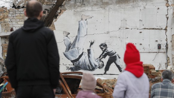 epa10303684 People watch a mural depicting child overthrowing a man in judo clothes, in a style resembling the works of British street artist Banksy, at a wall of a building that was destroyed during  ...