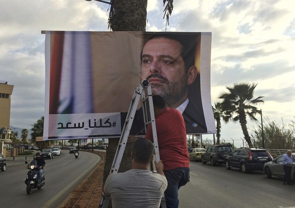 Workers hang a poster of outgoing Prime Minister Saad Hariri with Arabic words that read, &quot;We are all Saad,&quot; at a seaside street in Beirut, Lebanon, Thursday, Nov. 9, 2017. Hezbollah has cal ...