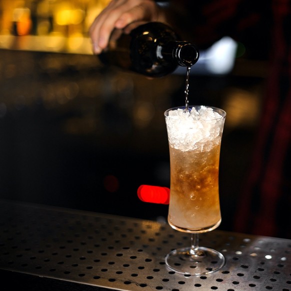 Barman pouring fresh tasty Sherry Cobbler drink into a cocktail glass on the bar counter trinken alkohol
