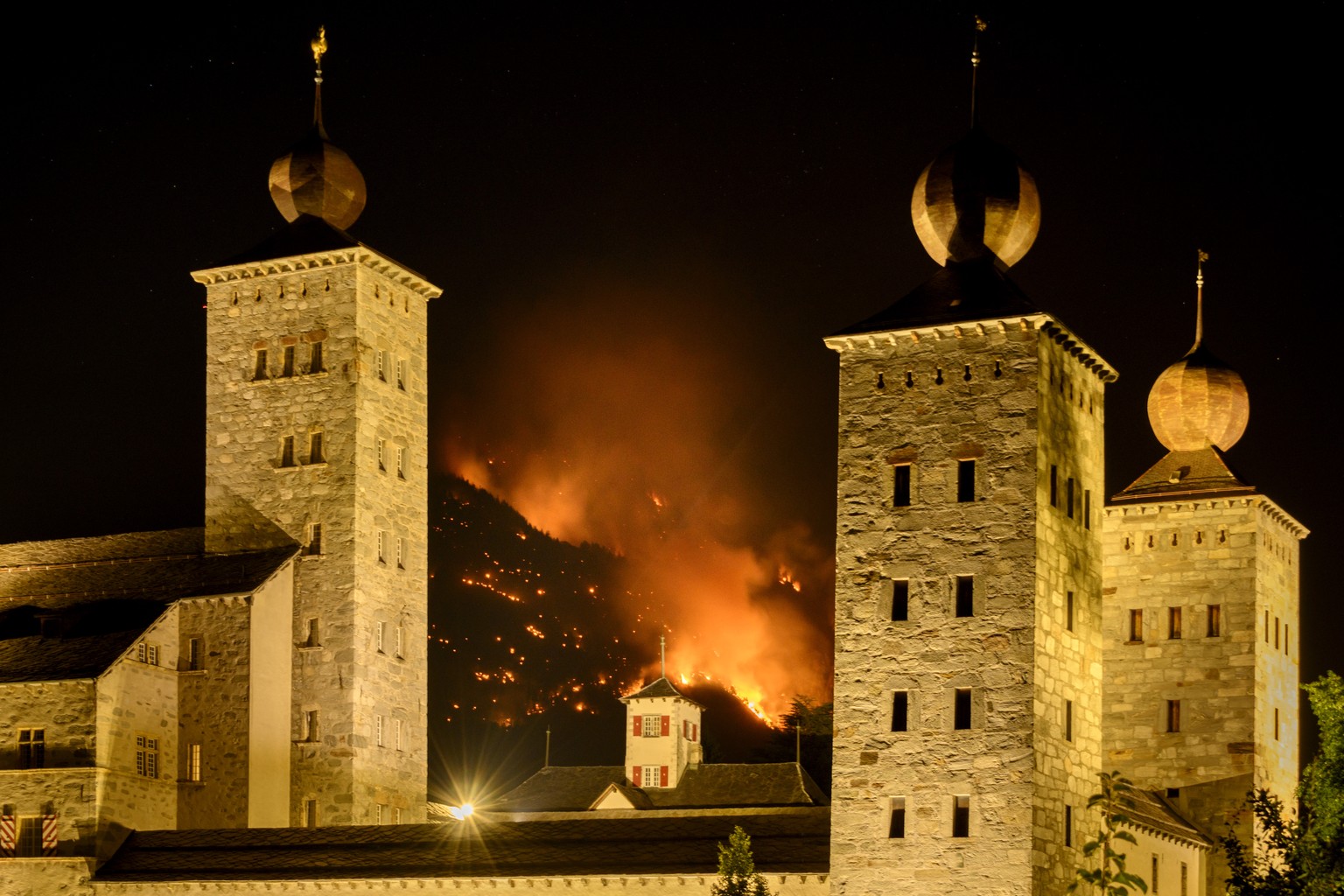 De la fumee et des flammes s&#039;echappent de la foret en feu au dessus des communes de Bitsch et Ried-Moerel ce lundi 17 juillet 2023 derriere le chateau Stockalper a Brig. Un incendie de foret s&#0 ...