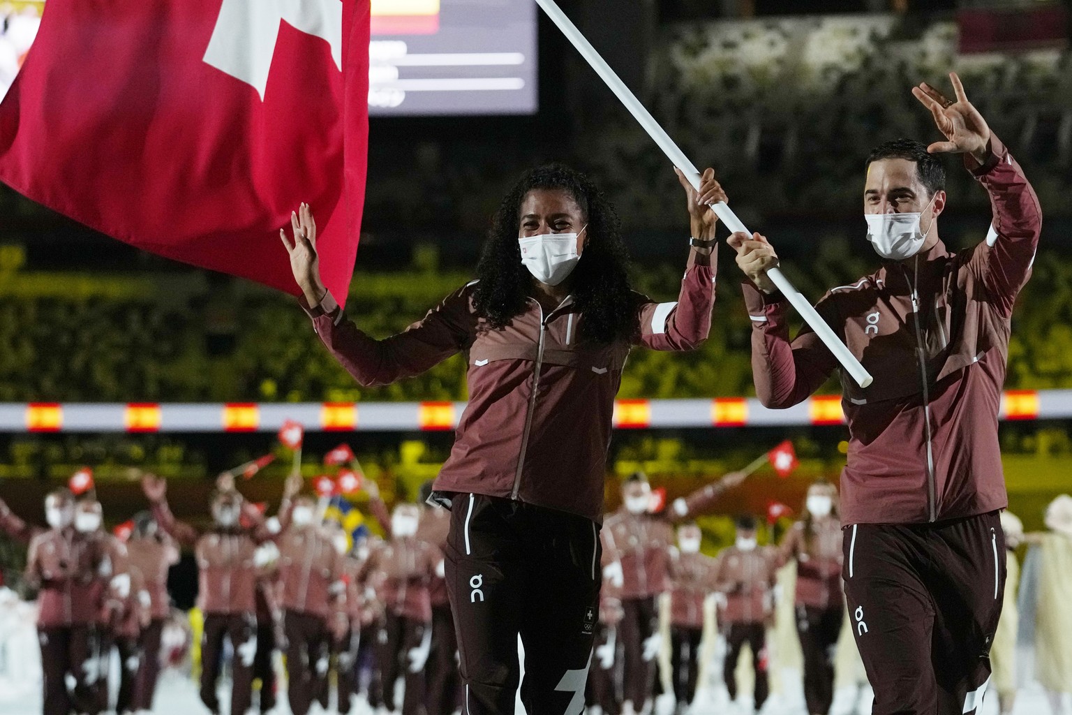 Mujinga Kambundji and Max Heinzer, of Switzerland, carry their country's flag during the opening ceremony in the Olympic Stadium at the 2020 Summer Olympics, Friday, July 23, 2021, in Tokyo, Japan. (A ...