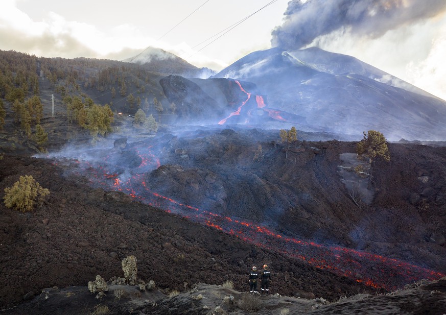 Firefighters look at lava flowing from a volcano on the Canary island of La Palma, Spain, Tuesday, Nov. 30, 2021. Several new volcanic vents opened in La Palma, releasing new lava that flowed fast dow ...